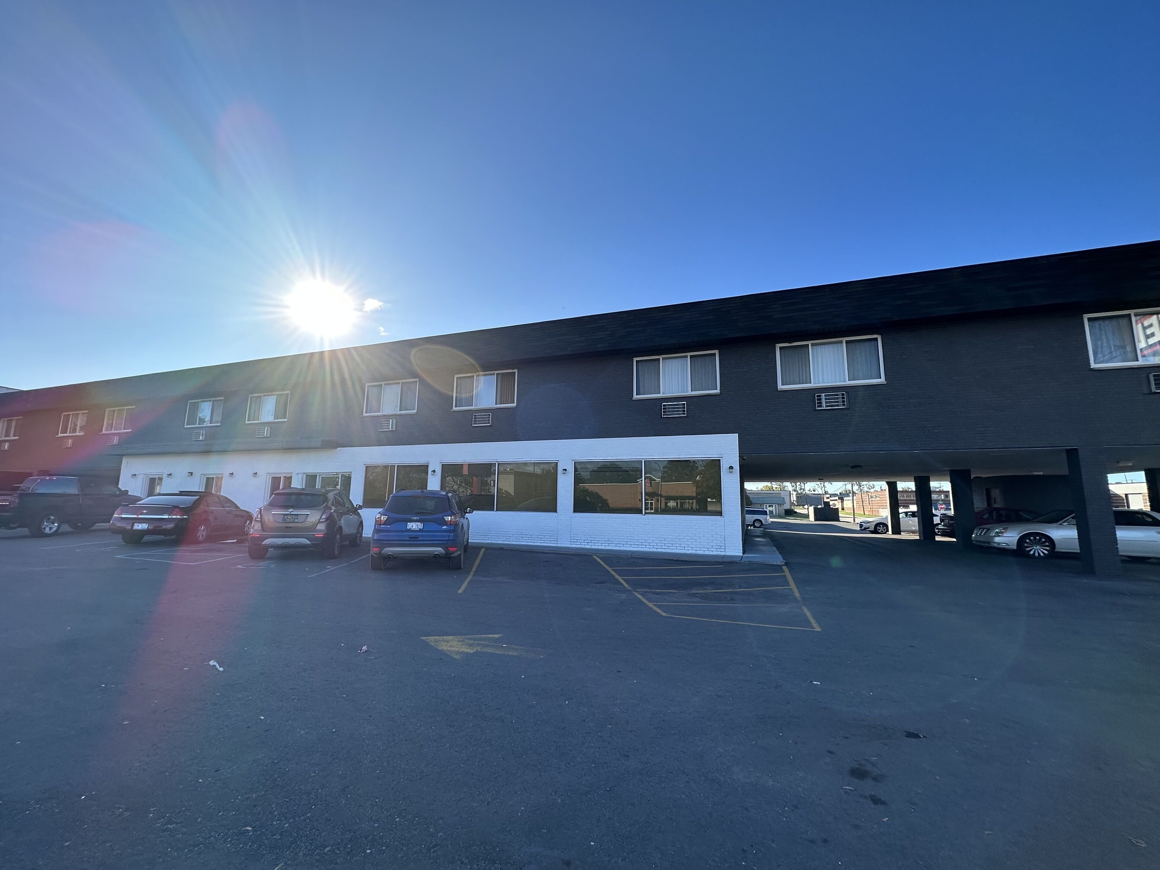 A parking lot with several cars, a building with multiple windows, and a clear sky.