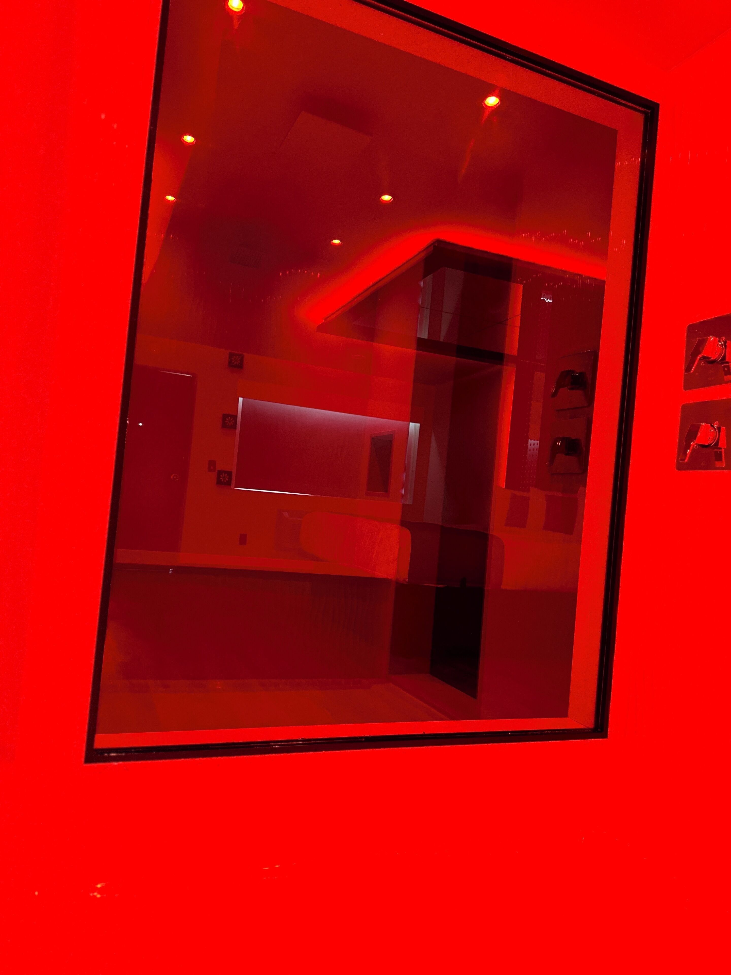A red-lit room with a glass partition, a bed, and a small table.