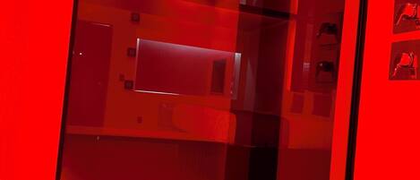 A red-lit room with a glass partition, a bed, and a small table.