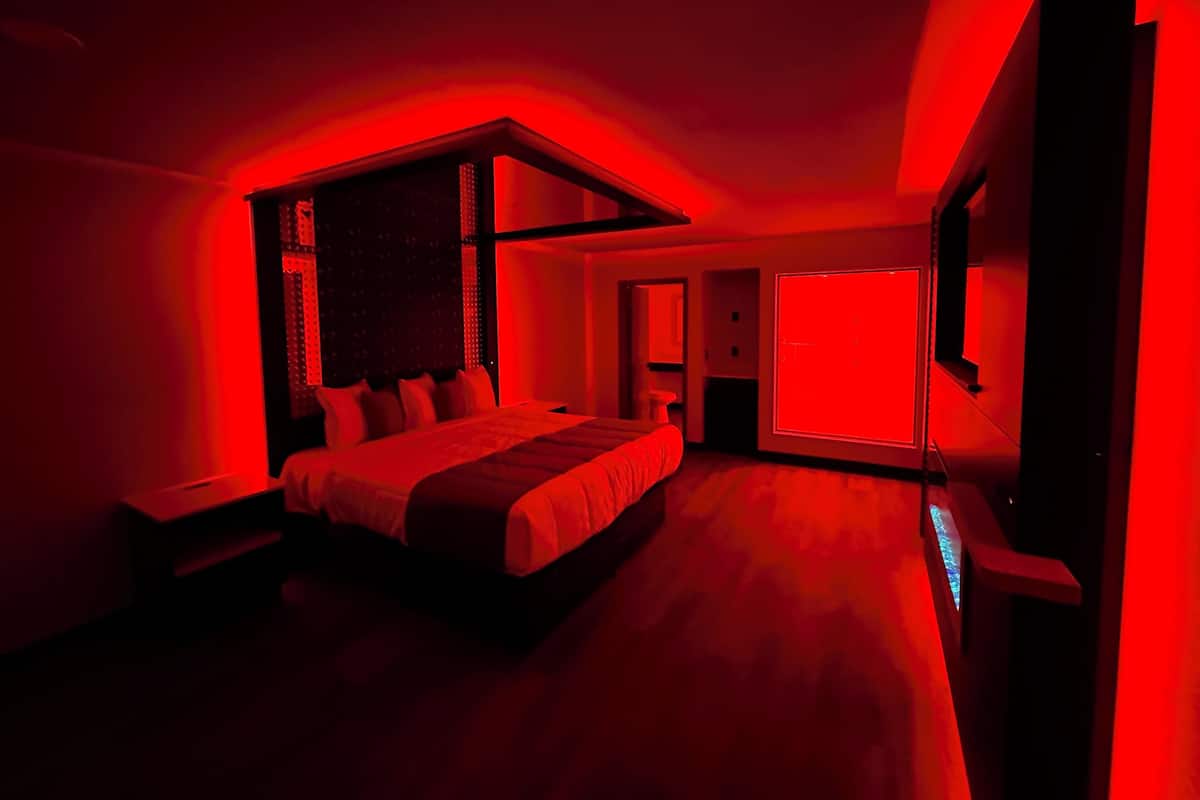 Une chambre moderne avec un grand lit, une télévision et un éclairage d’ambiance rouge.