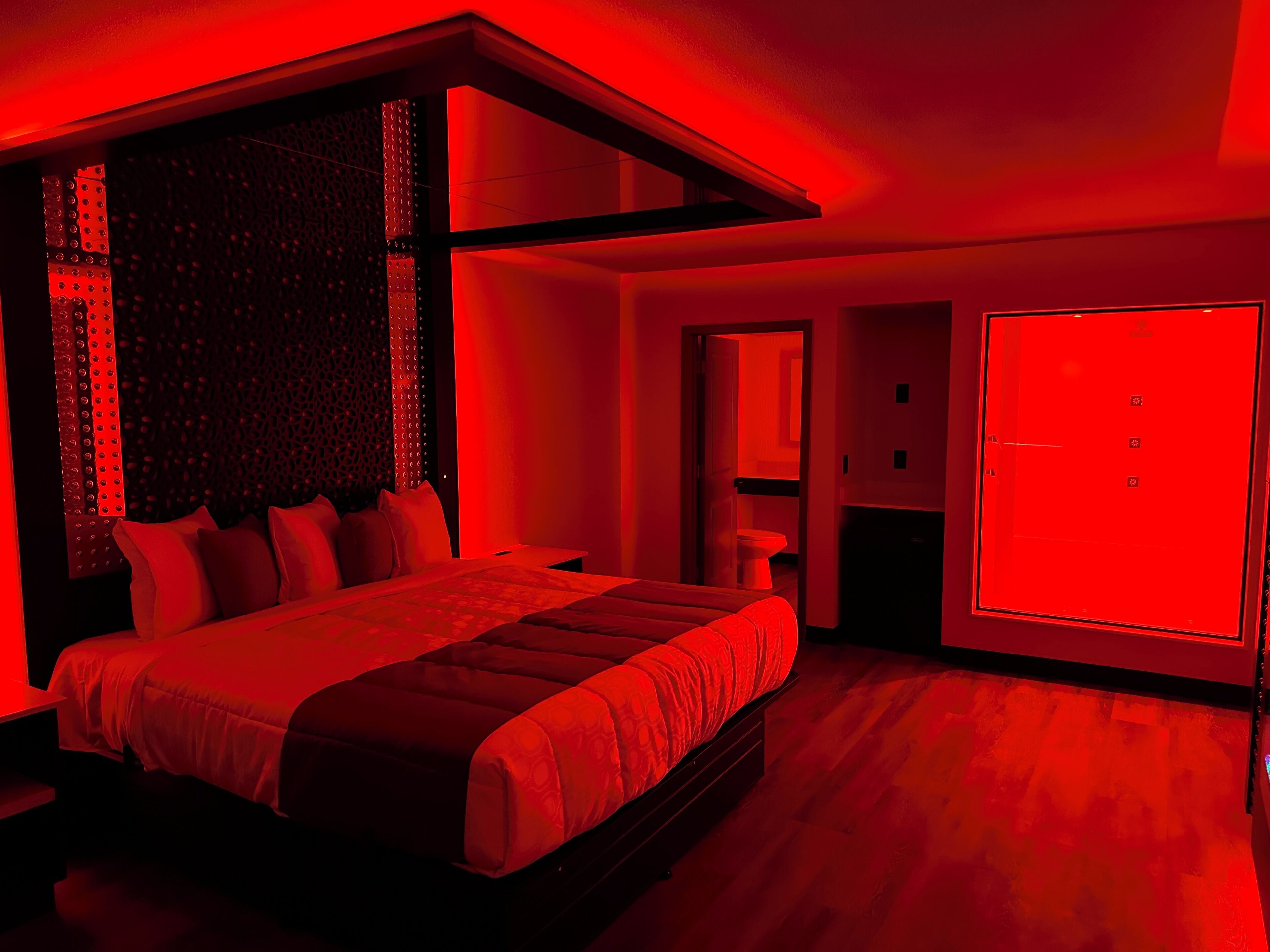 A modern bedroom with a large bed, a walk-in closet, and a red-lit bathroom.