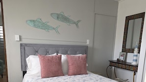 Un dormitorio con cabecera tapizada en gris, colcha estampada y decoración de peces en la pared.