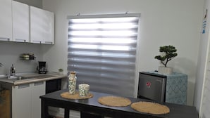 Una cocina compacta con armarios blancos, una mesa de comedor negra con dos sillas, una cafetera y una pequeña planta en maceta.