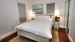 Un lit bien fait dans une pièce aux murs blancs, avec deux tables de chevet dotées de lampes et un tableau au-dessus du lit.