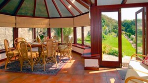 A covered patio with a table and chairs, a view of a garden, and a stone wall. - Slade Cottage (Bridgend)
