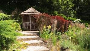 A garden pathway leading to a wooden gazebo with a thatched roof. - Slade Cottage (Bridgend)