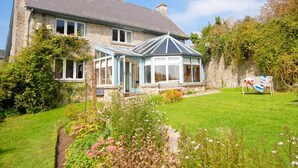 A stone house with a conservatory, surrounded by a well-maintained garden and a stone wall. - Slade Cottage (Bridgend)