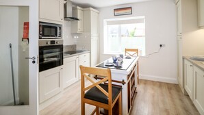 A compact kitchen with white cabinets, a microwave, oven, and a dining table with chairs. - Ahiohill Meadows (Aghyoghil Beg)