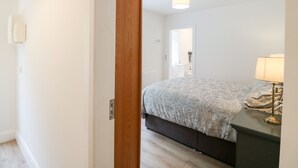 A bedroom with a bed, bedside table, lamp, and a door leading to a bathroom. - Ahiohill Meadows (Aghyoghil Beg)