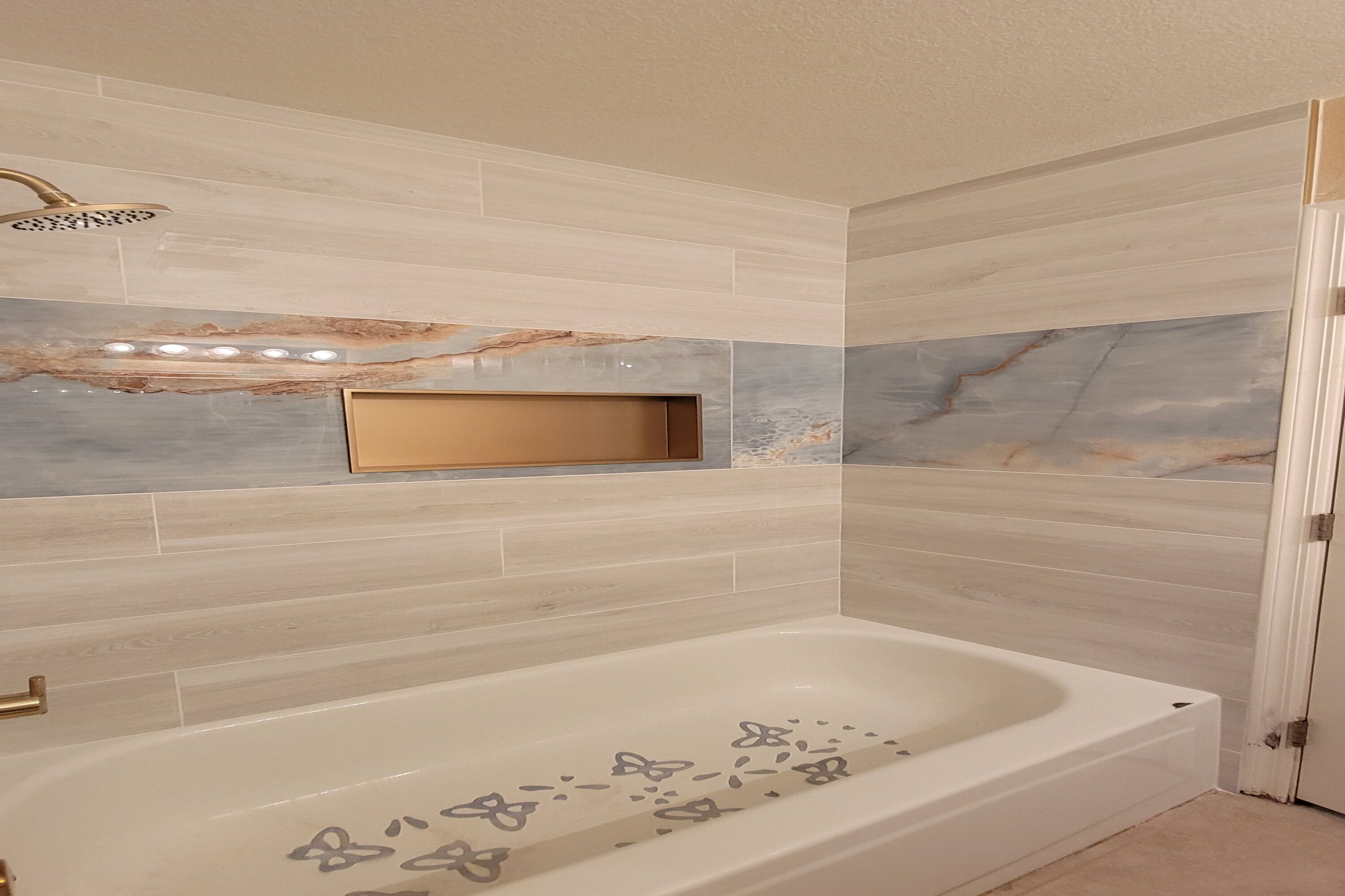 Une salle de bain moderne avec une baignoire sur pieds, des carreaux de marbre aux murs et un éclairage encastré.