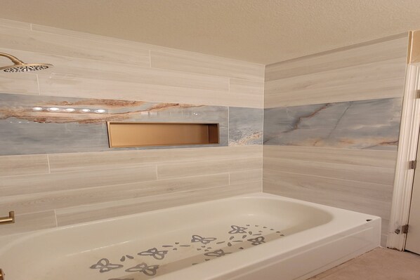 A modern bathroom with a freestanding bathtub, marble wall tiles, and recessed lighting.