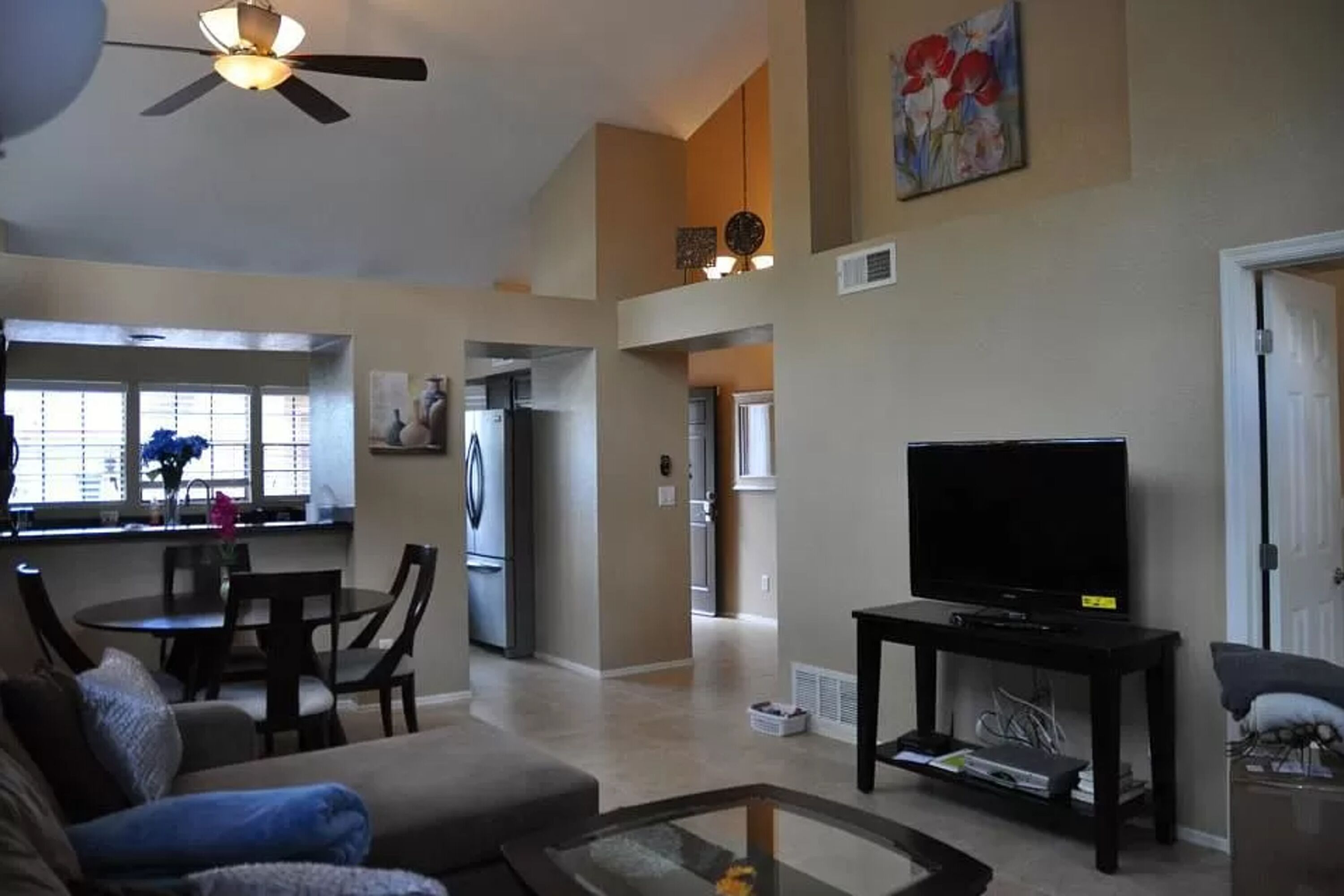 A spacious living room with a large flat-screen TV, a dining area with a table and chairs, and a kitchen in the background.