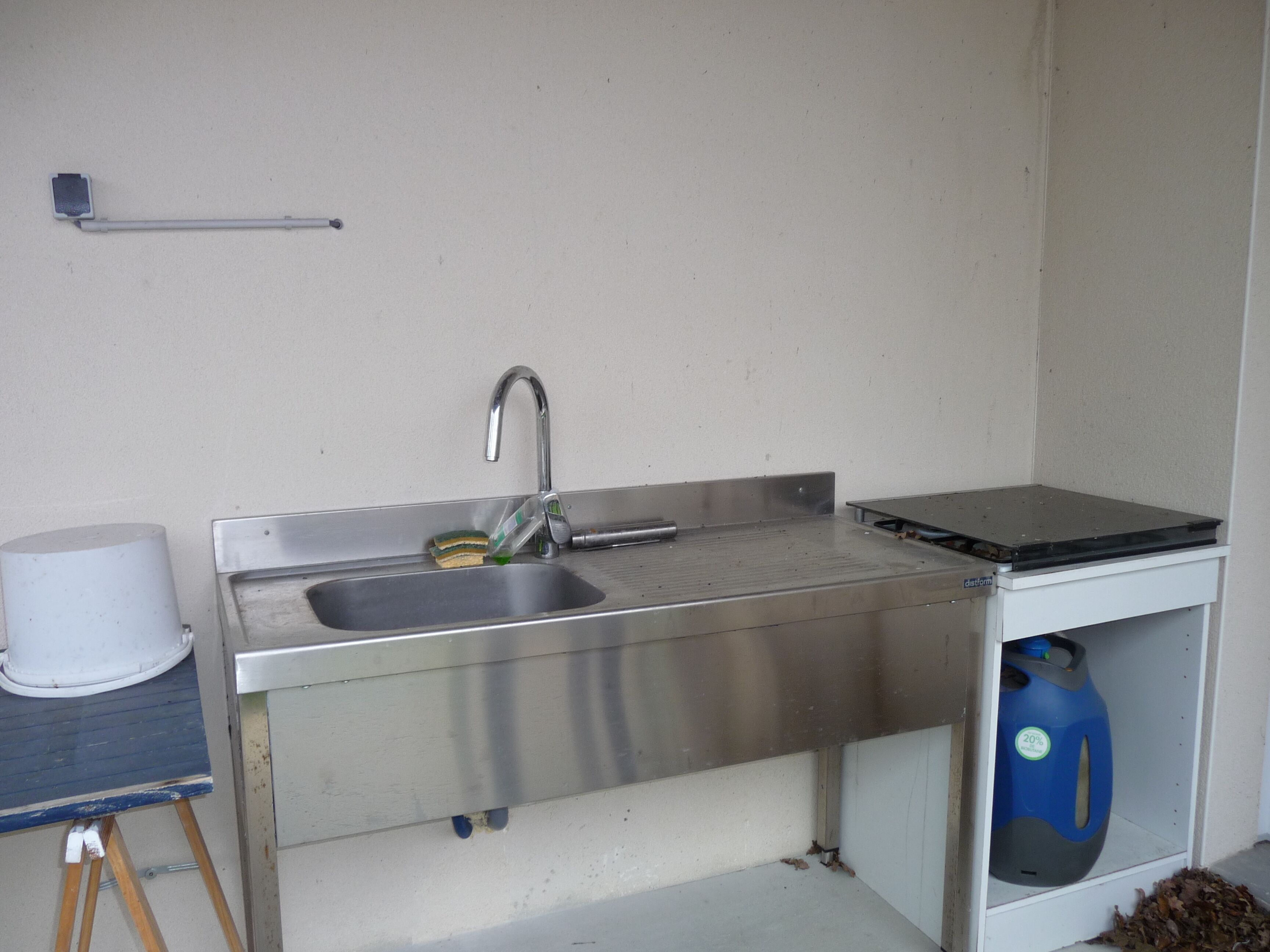 Una cuina petita amb un rentaplatets d'acer inoxidable, un dispensador d'aigua blau i un taulell blanc.