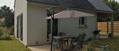 A single-story house with a patio area featuring a table and chairs, a covered seating area, and a small window.