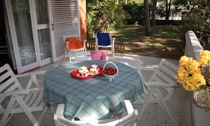 Une terrasse avec une table dressée pour un repas, entourée de chaises blanches, et donnant sur un jardin.