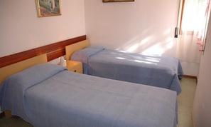 A hotel room with two single beds, a wooden headboard, a bedside table with a lamp, and a painting on the wall.