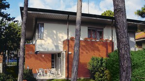 Uma casa moderna com dois andares, um alpendre, uma área de estar coberta ao ar livre e um pequeno jardim.