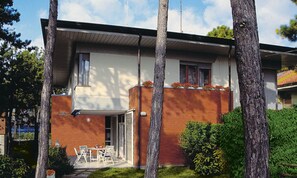 A modern two-story house with a patio area featuring a table and chairs. - Centric Villa in Lignano Pineta (Lignano Sabbiadoro)