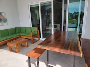 Un salon moderne avec une table à manger en bois, un canapé vert et une porte-fenêtre en verre donnant sur un espace extérieur.