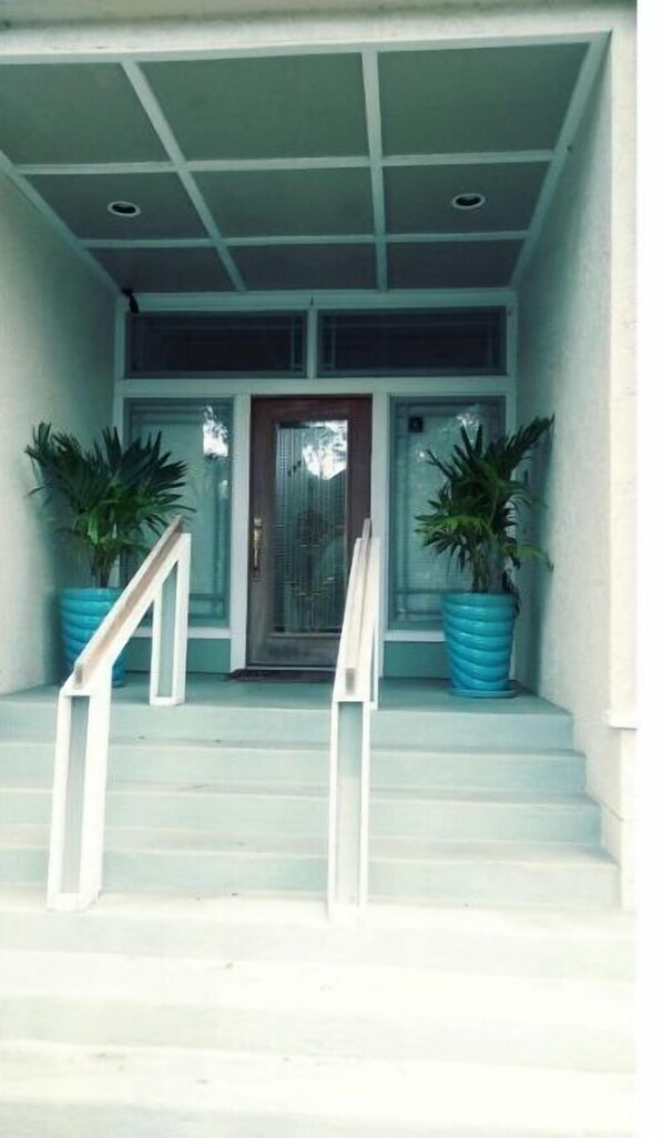 Staircase leads to a front door flanked by large potted plants.
