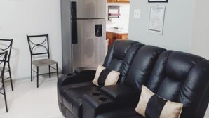 A modern living room with a black leather sofa, two chairs, a refrigerator, and a kitchen area in the background. - Cozy updated family sized Condo just Minutes from Ocho Rios (Tower Isle)