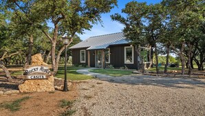 Une cabane rustique appelée Rocky Ridge Casita, avec une allée en gravier, entourée d’arbres et bordée d’une pelouse bien entretenue.