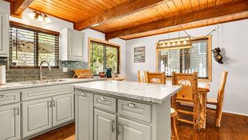 A kitchen with a central island, wooden ceiling beams, and a dining area with a wooden table and chairs.