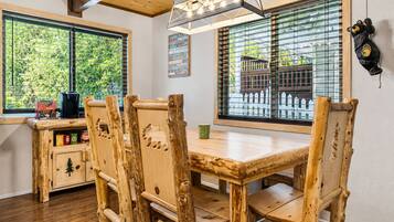A rustic wooden dining area with a table and chairs, a hanging light fixture, and a view of greenery outside.