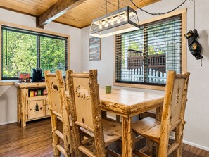 Ein rustikaler Essbereich aus Holz mit Tisch und Stühlen, einer Hängeleuchte und Blick ins Grüne.