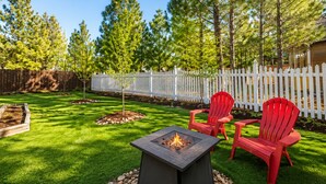 Un patio trasero con un brasero, sillas Adirondack rojas y una cerca blanca de piquetes.