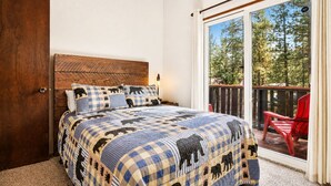 Un dormitorio con colcha a cuadros, cabecero de madera y vistas a un balcón con una silla roja.