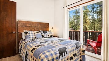 Ein Schlafzimmer mit kariertem Bettbezug, einem Holzkopfteil und Blick auf einen Balkon mit einem roten Stuhl.