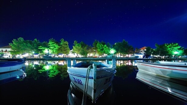 A nighttime marina with boats docked, trees illuminated by street lamps, and a calm water surface reflecting the lights. - Studio apartment in Sukošan with Air condition, WIFI (5102-2) (Sukošan)