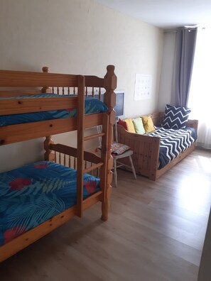 Quarto com beliches, uma secretária de madeira e um sofá com almofadas estampadas.