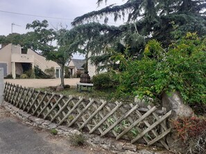 Un espace extérieur clos, avec un chemin de gravier, un banc en bois et un mur en pierre.