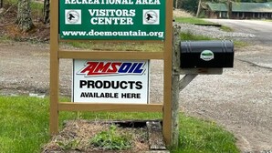 A sign for Doe Mountain Recreational Area Visitors Center with a mailbox and AMSOIL products available. - Forest Getaway (Mountain City)