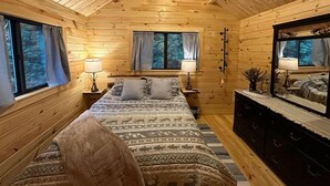 A cozy log cabin bedroom with a bed, two bedside tables, a dresser, and a mirror. - Forest Getaway (Mountain City)