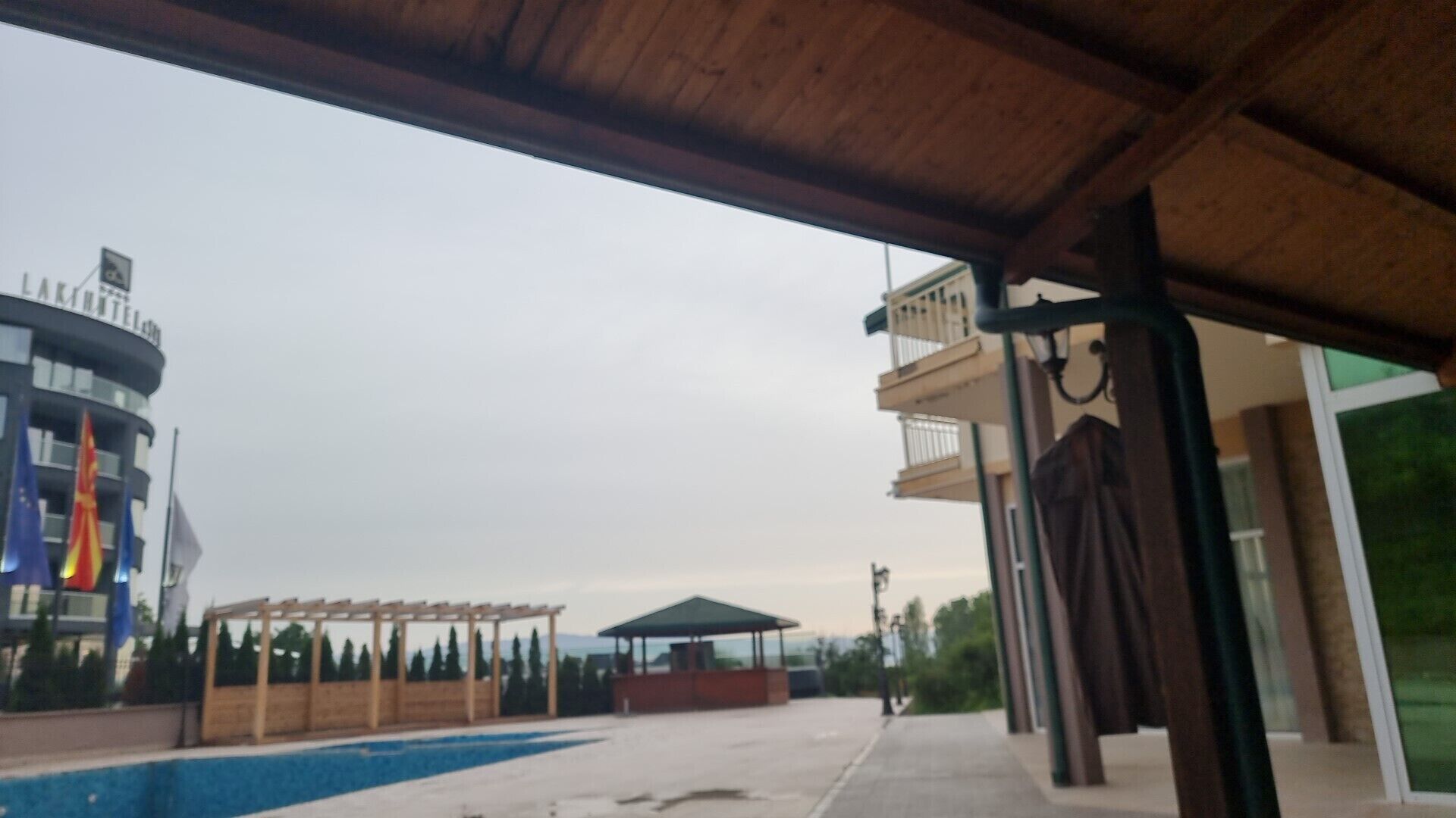 A covered outdoor area with a pool, a pergola, and a building with balconies.