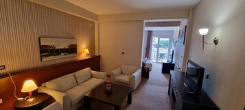 Habitación de hotel con sofá, sillones, una mesita de centro, televisor y lámpara.