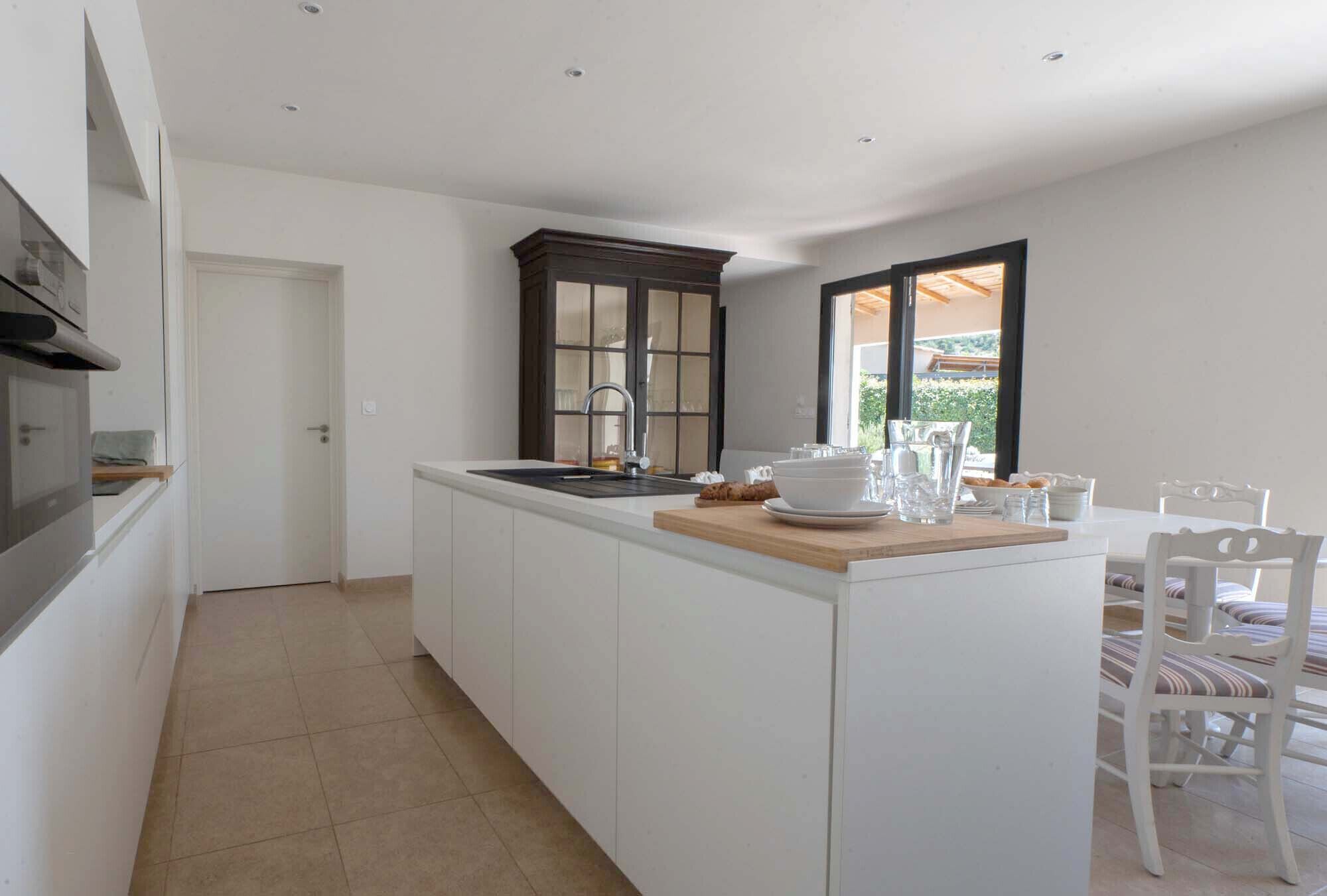 A modern kitchen with white cabinetry, a dark wooden cabinet, and a dining area with white chairs.