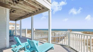 Un espace extérieur abrité comprenant deux chaises longues turquoise et une balustrade blanche donnant sur la plage.