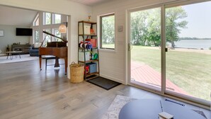 A spacious living room with a grand piano, a television, and a large window overlooking a grassy area. - Lakefront Sunburg Vacation Rental w/ Boat Dock! (Sunburg)