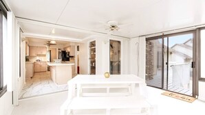 Eine geräumige Terrasse mit einem weißen Tisch, einem Deckenventilator und einer Schiebetür zum Garten.