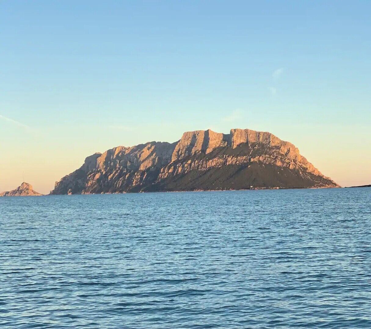 Eine Küstenlandschaft mit einer markanten Felseninsel und ruhigem Meer.