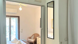 Un dormitorio con cama, una silla, un aparador y un espejo. Hay una puerta que da a otra habitación.
