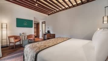 Una habitación de hotel con una cama, dos sillones tapizados, una mesita y un televisor montado en la pared.