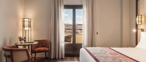 Une chambre d’hôtel avec un lit, un coin salon comprenant une chaise et une petite table, une lampe, et une vue par la fenêtre.