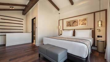 Un dormitorio moderno con una cama grande, una banca, vigas de madera y obras de arte en la pared.