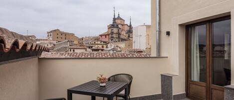 A balcony with a table and chairs, overlooking a cityscape with historical buildings.