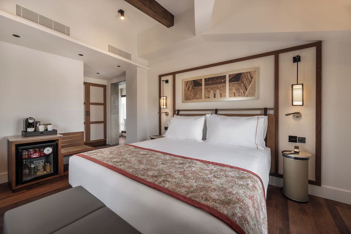 Una habitación de hotel con una cama grande, mesita de noche y un refrigerador pequeño.